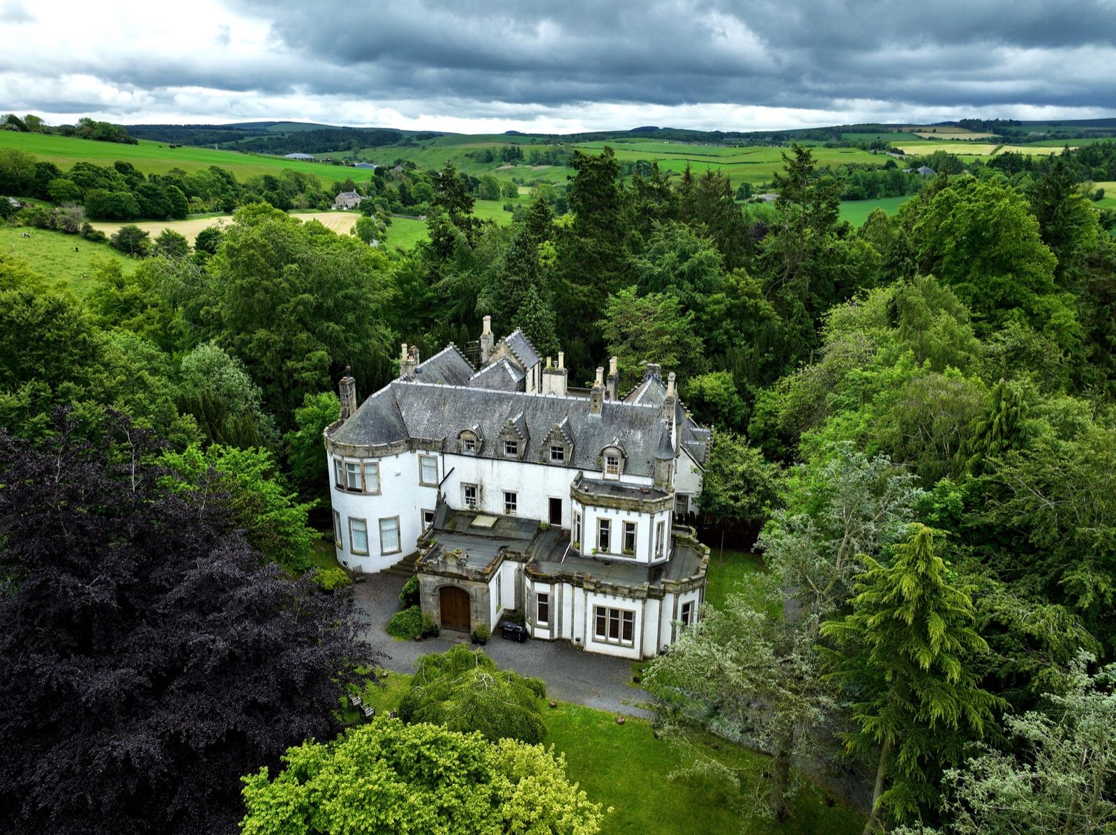 Harvieston Hall in Midlothian, seen from above among mature trees — the group's Scottish origin.
